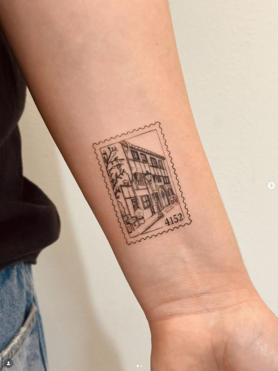 Tattoo einer Briefmarke mit einer detaillierten Hausansicht auf dem Unterarm